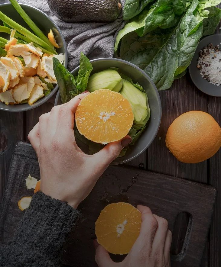 Hands preparing fresh oranges and vegetables